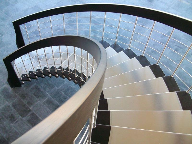 Escalier courbe suspendu de type nova.Main_courantes débillardées en bois lamellé-collé. Marches en bois recouvertes de tôles inox. balustres et lisses en inox.